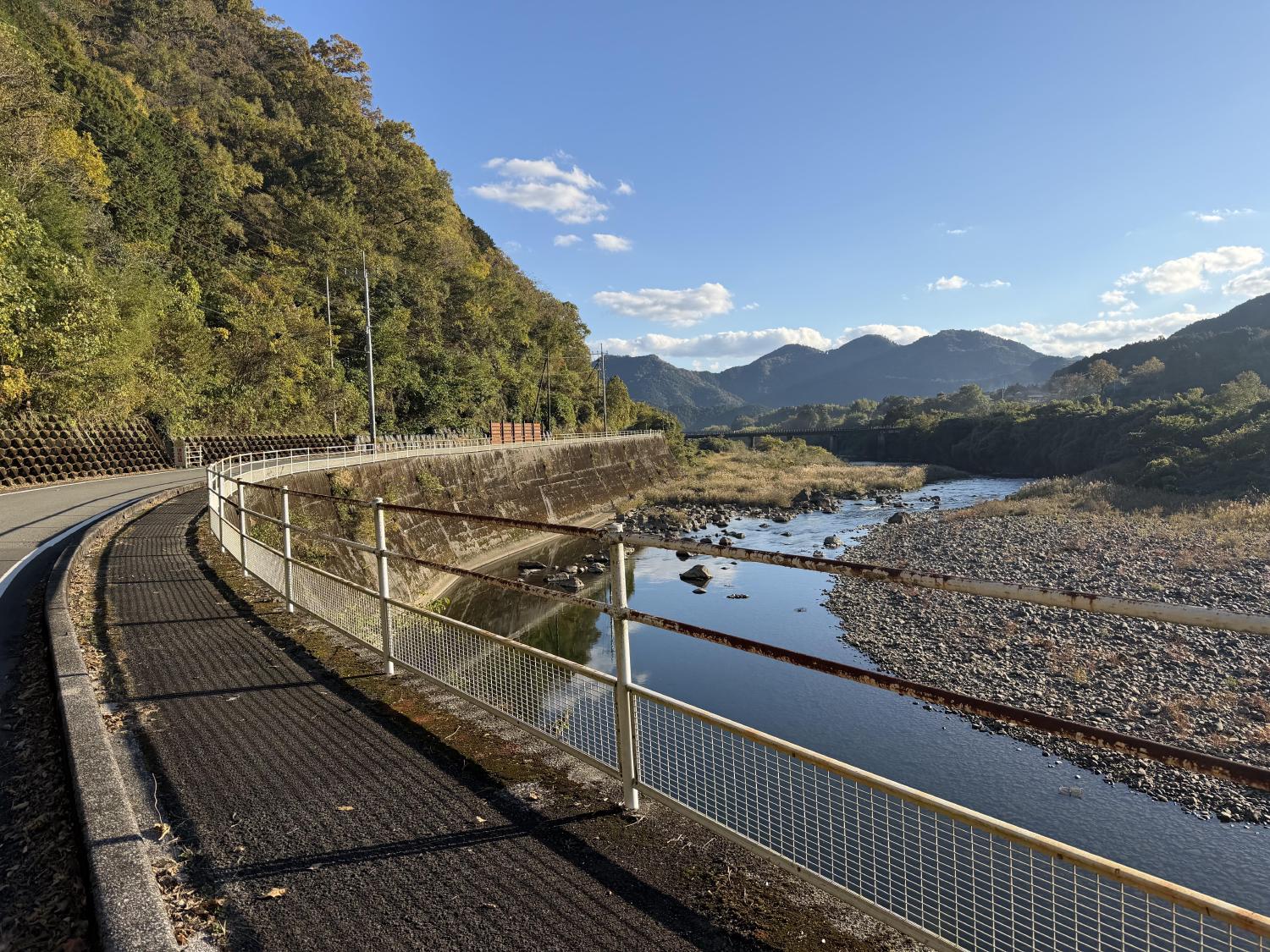 Riverside cycling road winding beneath mountains under blue sky